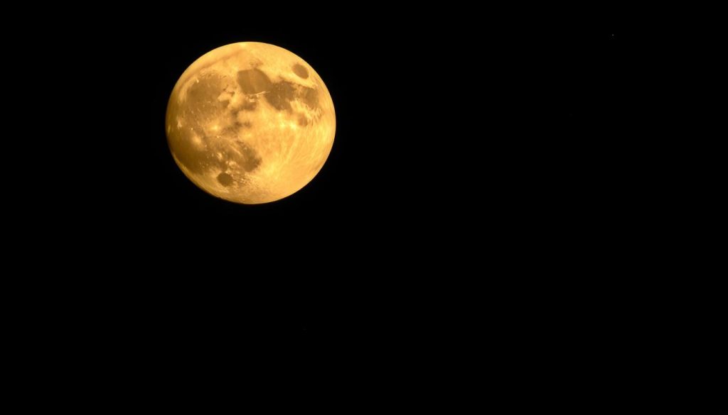 A dramatic, highly detailed full moon rising in a clear night sky. The moon's surface is textured and cratered, with a warm, golden-orange glow illuminating the foreground. In the middle ground, silhouetted trees and mountains create a serene, natural landscape. The background is a deep, inky blue-black sky, dotted with twinkling stars. The overall mood is one of tranquility, mysticism, and awe-inspiring natural beauty. Soft, diffused lighting creates a sense of depth and dimension, while a wide-angle lens captures the grandeur of the scene. This image evokes the mysterious power and allure of the full moon, perfect for illustrating a section on lunar events.